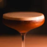 A classic Between the Sheets cocktail in a coupe glass with a lemon twist on a bar.