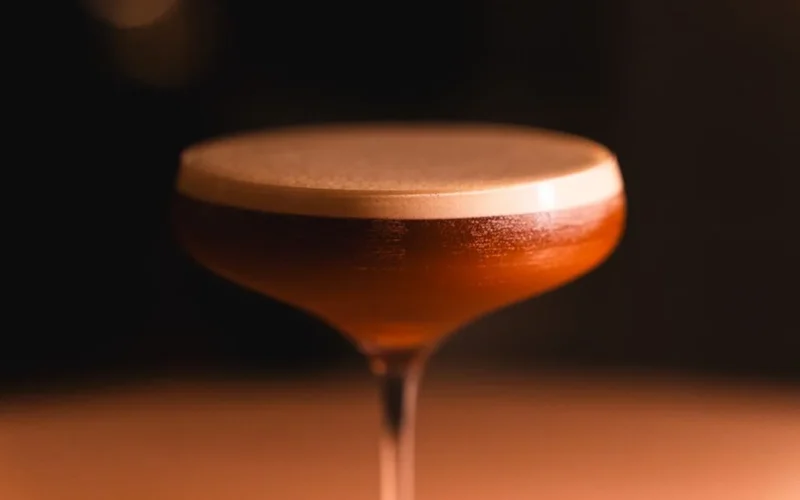 A classic Between the Sheets cocktail in a coupe glass with a lemon twist on a bar.