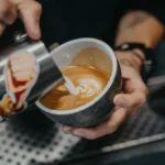 Close up of a barista pouring milk into a coffee cup in a modern cafe.