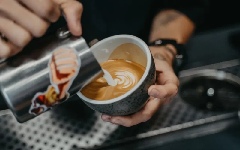Close up of a barista pouring milk into a coffee cup in a modern cafe.