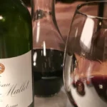 A bottle of red wine and a filled glass on a restaurant table.