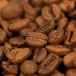 A steaming cup of unsweetened black coffee with roasted beans on a wooden surface.