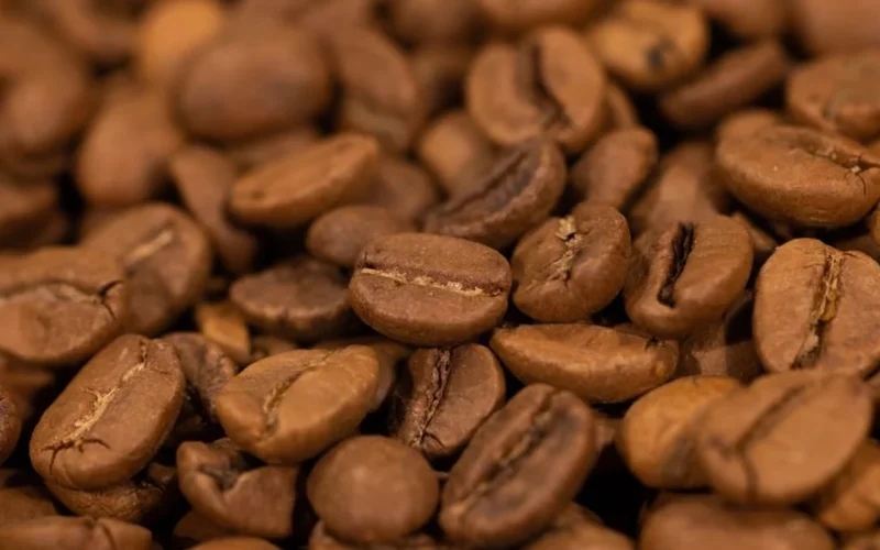 A steaming cup of unsweetened black coffee with roasted beans on a wooden surface.