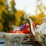 Close-up of an antique ceramic teapot and teacup with loose tea leaves on wood.