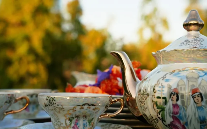 Close-up of an antique ceramic teapot and teacup with loose tea leaves on wood.