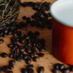 Clear water in a glass beaker next to roasted coffee beans on a dark surface.