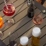 An orange Aperol spritz cocktail with ice and orange slices on a sunlit outdoor table.
