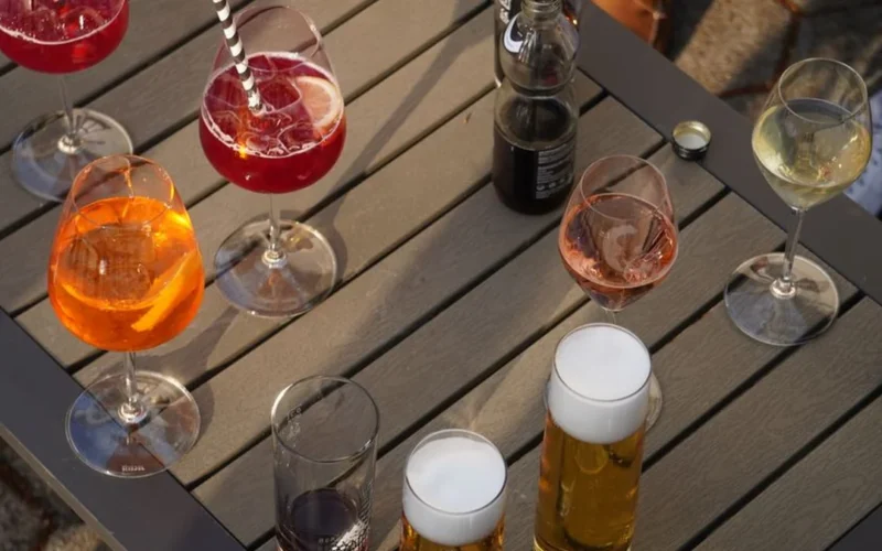An orange Aperol spritz cocktail with ice and orange slices on a sunlit outdoor table.