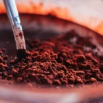 A cup of black coffee next to a bowl of dark cocoa powder on stone.