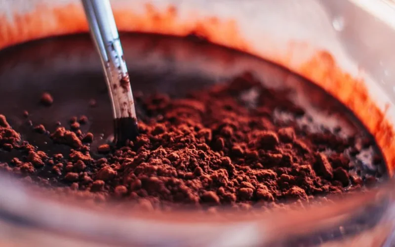 A cup of black coffee next to a bowl of dark cocoa powder on stone.