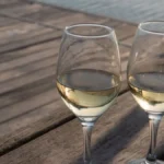 A glass of golden Chardonnay wine resting on a wooden table next to acacia wood.