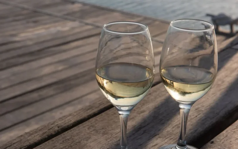 A glass of golden Chardonnay wine resting on a wooden table next to acacia wood.