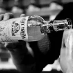A clear glass bottle of Mexican spirit on a stone bar with hibiscus and cacao.