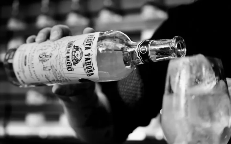 A clear glass bottle of Mexican spirit on a stone bar with hibiscus and cacao.