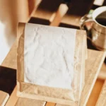 Overhead view of a white coffee cup and single-origin coffee bag on a light wood table.
