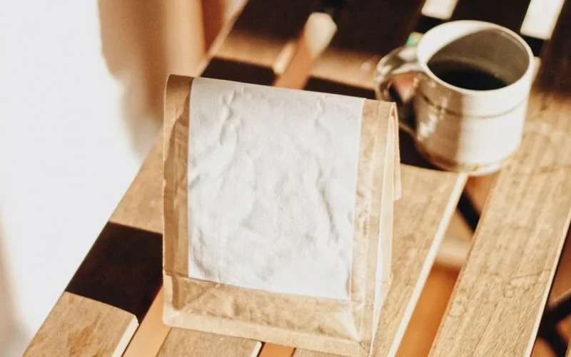Overhead view of a white coffee cup and single-origin coffee bag on a light wood table.