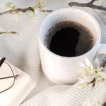 Black coffee in a ceramic cup on a wooden table with spring morning sunlight.