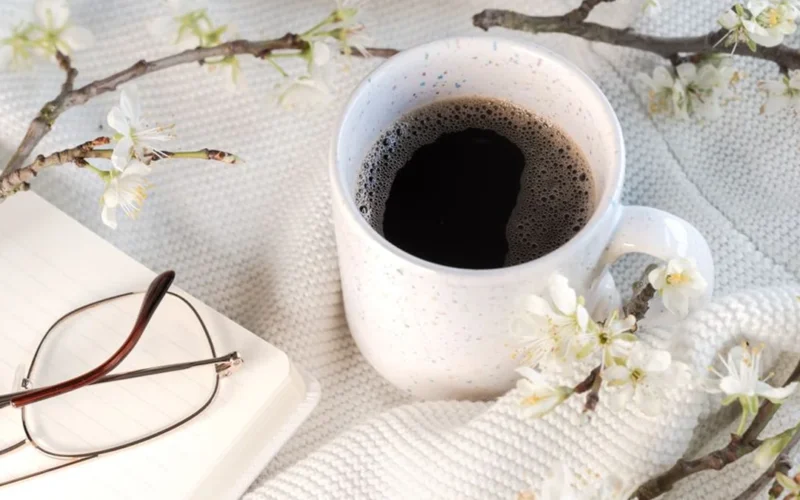 Black coffee in a ceramic cup on a wooden table with spring morning sunlight.