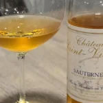 A glass of golden Sauternes dessert wine on a wooden table with sliced stone fruit.