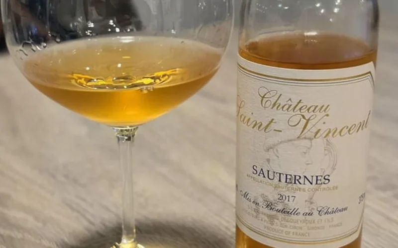 A glass of golden Sauternes dessert wine on a wooden table with sliced stone fruit.