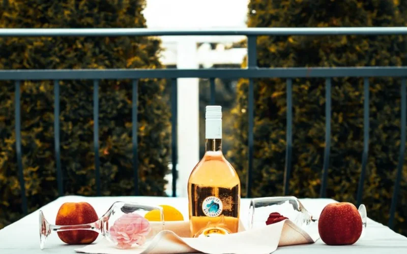 A bottle and glass of vibrant pink Saperavi rosé wine on a wooden surface.
