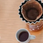 A glass carafe and ceramic mug of dark black coffee on a stone surface.