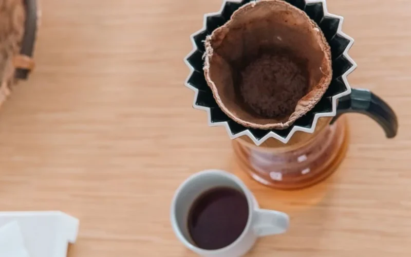 A glass carafe and ceramic mug of dark black coffee on a stone surface.