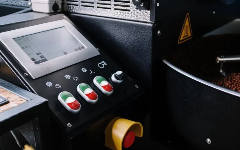 A professional stainless steel M-Series coffee roaster with a digital touchscreen interface in a production facility.