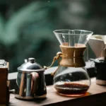 Overhead view of manual coffee brewers, Chemex, and roasted coffee beans on a dark surface.