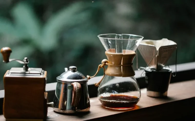 Overhead view of manual coffee brewers, Chemex, and roasted coffee beans on a dark surface.