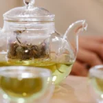 A glass teapot filled with green tea sitting on a stone kitchen countertop.