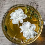Close-up of jasmine pearl tea leaves swirling in a glass mug of hot water.