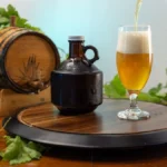 A glass of amber cider resting on a wooden barrel next to fresh apple slices.