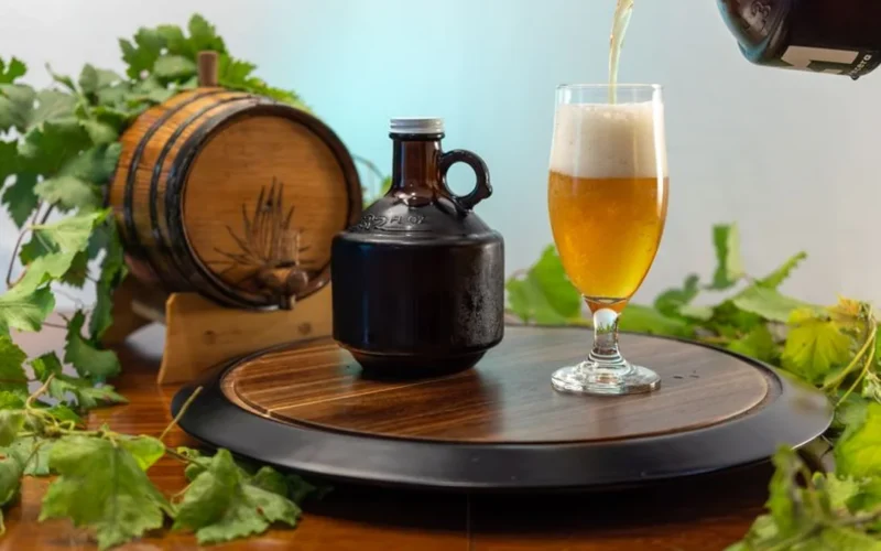 A glass of amber cider resting on a wooden barrel next to fresh apple slices.