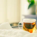 Overhead view of green Longjing tea in a glass mug on a wooden table.