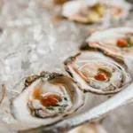 A silver platter of fresh oysters on crushed ice with lemon wedges and mignonette.