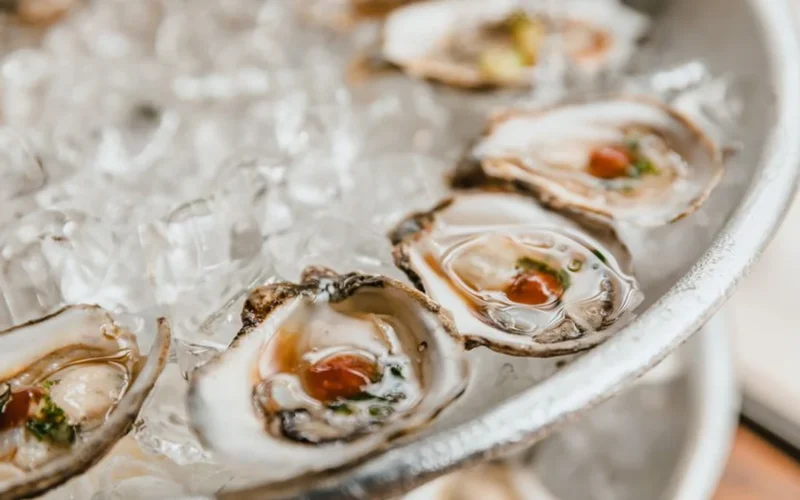 A silver platter of fresh oysters on crushed ice with lemon wedges and mignonette.