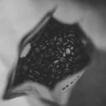 Overhead view of a coffee bag with beans and a silver spoon on marble.