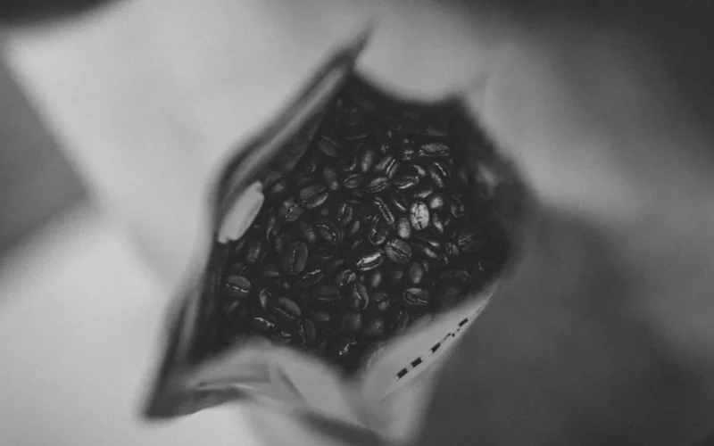 Overhead view of a coffee bag with beans and a silver spoon on marble.