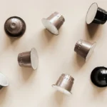 Aluminum and paper coffee capsules resting on a dark stone countertop surface.