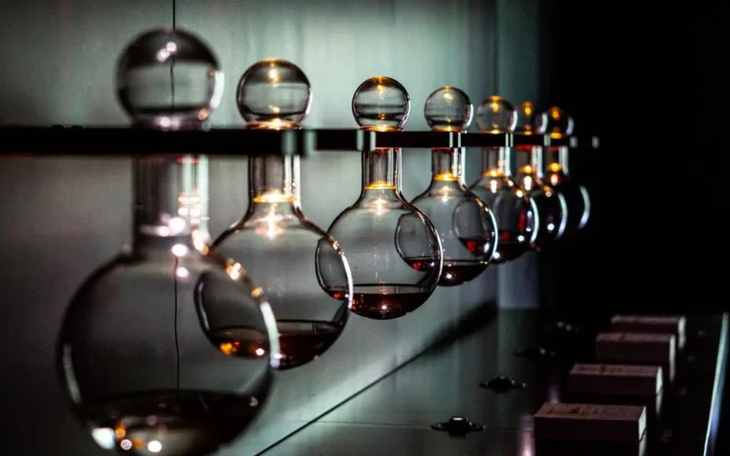 Chardonnay wine bottles and a glass of amber wine next to scientific laboratory glassware.