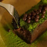 Sliced matcha sponge cake with chocolate ganache on a white marble surface.