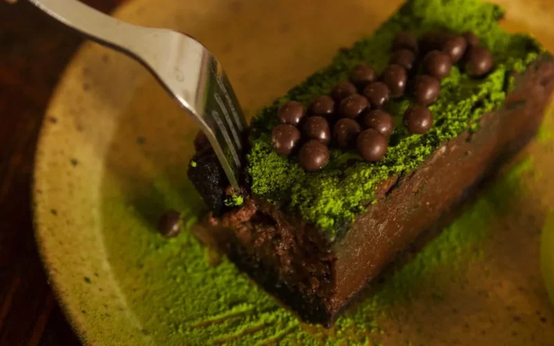 Sliced matcha sponge cake with chocolate ganache on a white marble surface.