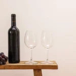 Red wine bottles and glasses on a dark wooden surface with dried vine leaves.