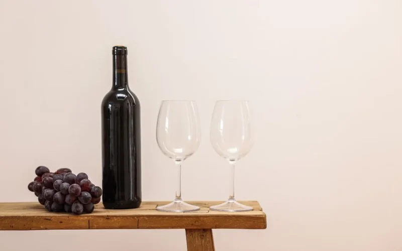 Red wine bottles and glasses on a dark wooden surface with dried vine leaves.