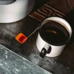 Overhead view of steaming black tea in a dark ceramic cup on a wooden surface.