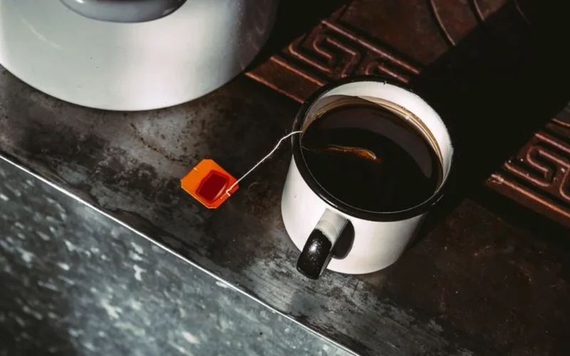 Overhead view of steaming black tea in a dark ceramic cup on a wooden surface.
