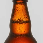 Close-up of water droplets on a dark amber glass spirit bottle on a bar.