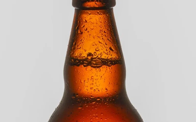 Close-up of water droplets on a dark amber glass spirit bottle on a bar.