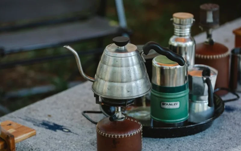 Overhead view of an insulated mug, immersion heater, and coffee beans on a flat surface.